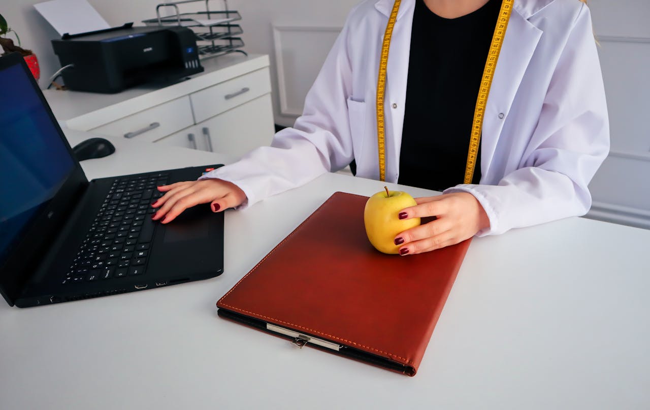 A dietician sitting at a desk with a laptop and apple, symbolizing healthy working lifestyle.