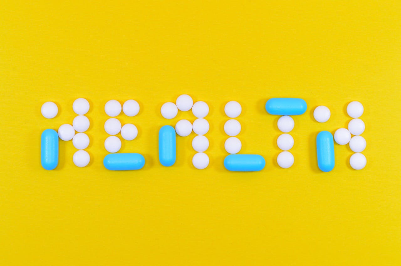 Pills spelling health on a vibrant yellow background, symbolizing wellness.